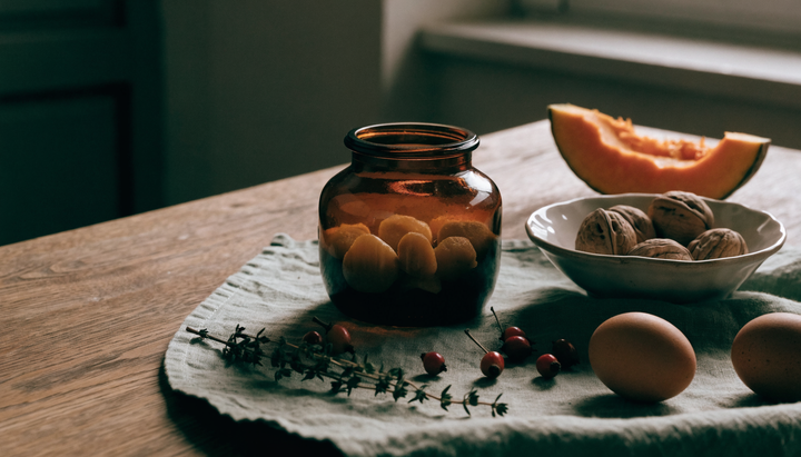 Ce vitamine să iei toamna: borcan de sticlă cu jeleuri, nuci, măceșe, ouă și o felie de dovleac așezate pe o pânză de in, pe o masă de lemn, în lumină de dimineață.