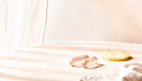 Cel mai bun probiotic: două capsule vegetale așezate lângă o felie subțire de ananas, pe o suprafață crem, în lumină difuză de dimineață